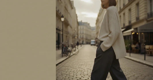 Woman in a minimalist neutral-toned outfit — a relaxed knit and tailored trousers, crossing a sunlit Paris side street in...