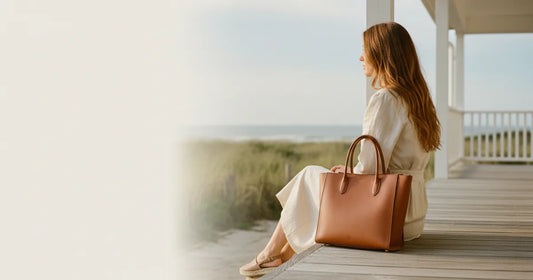 Woman holding a structured leather tote, shot from behind, sitting on the edge of a Hamptons clapboard porch