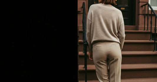Woman in a minimalist neutral-toned outfit — a relaxed knit and tailored trousers, leaning against a Brooklyn brownstone s...