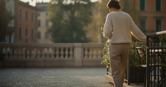 Woman in a minimalist neutral-toned outfit — a relaxed knit and tailored trousers, stepping off a Milan trattoria terrace...
