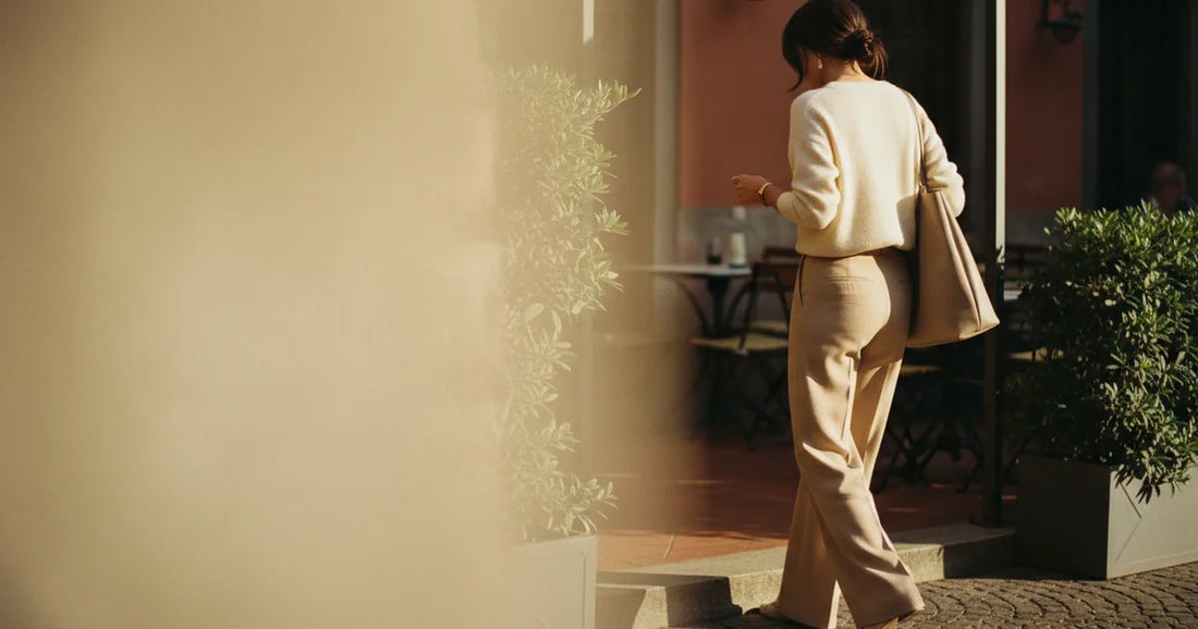 Woman in a minimalist neutral-toned outfit — a relaxed knit and tailored trousers, stepping off a Milan trattoria terrace...