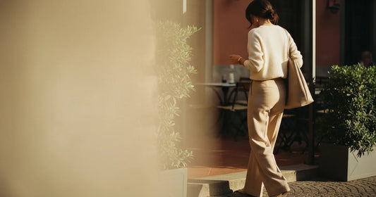 Woman in a minimalist neutral-toned outfit — a relaxed knit and tailored trousers, stepping off a Milan trattoria terrace...