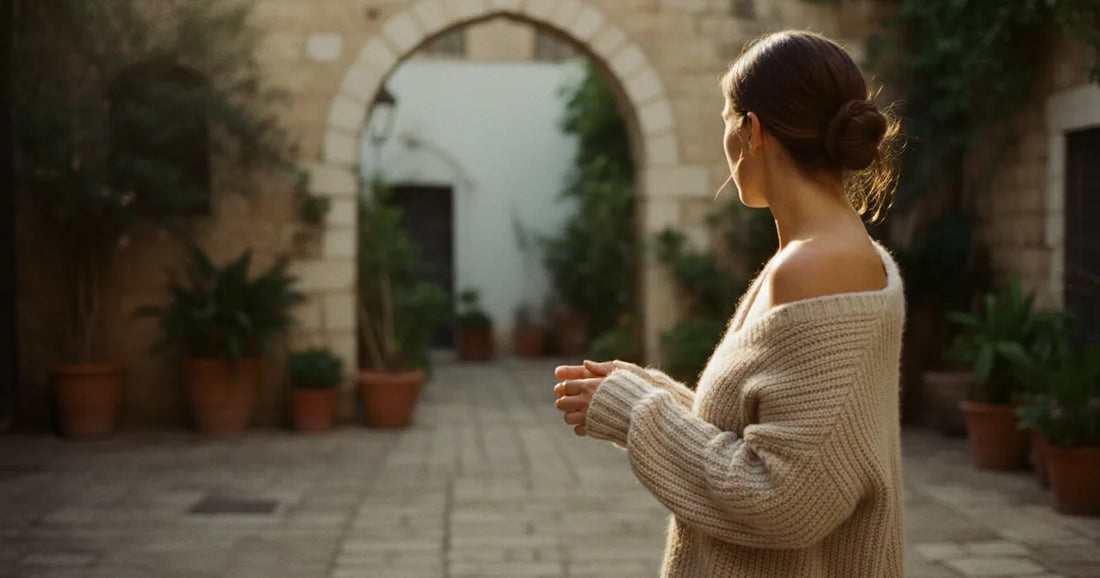Woman in a chunky oatmeal knit sweater, pausing at a sunlit Tel Aviv courtyard