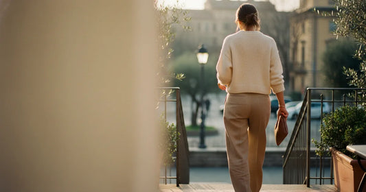 Woman in a minimalist neutral-toned outfit — a relaxed knit and tailored trousers, stepping off a Milan trattoria terrace...