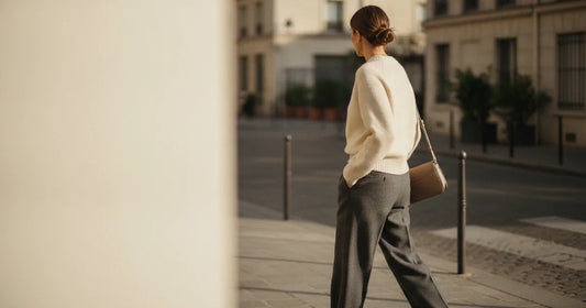 Woman in a minimalist neutral-toned outfit — a relaxed knit and tailored trousers, crossing a sunlit Paris side street in...