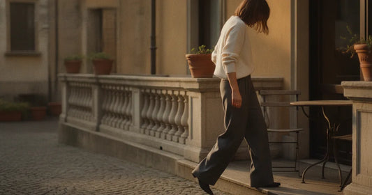 Woman in a minimalist neutral-toned outfit — a relaxed knit and tailored trousers, stepping off a Milan trattoria terrace...