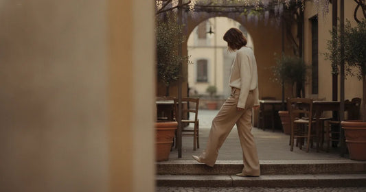 Woman in a minimalist neutral-toned outfit — a relaxed knit and tailored trousers, stepping off a Milan trattoria terrace...